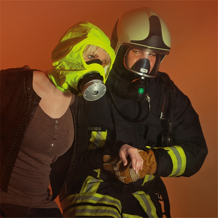 Trainingsschutzhaube Parat 5510 im Einsatz Person trägt gelbe Schutzhaube mit Atemfilter neben Feuerwehrmann.