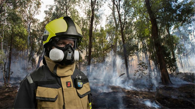 Feuerwehrmann in Schutzkleidung und Atemmaske vor rauchigem Waldbrand-Hintergrund.