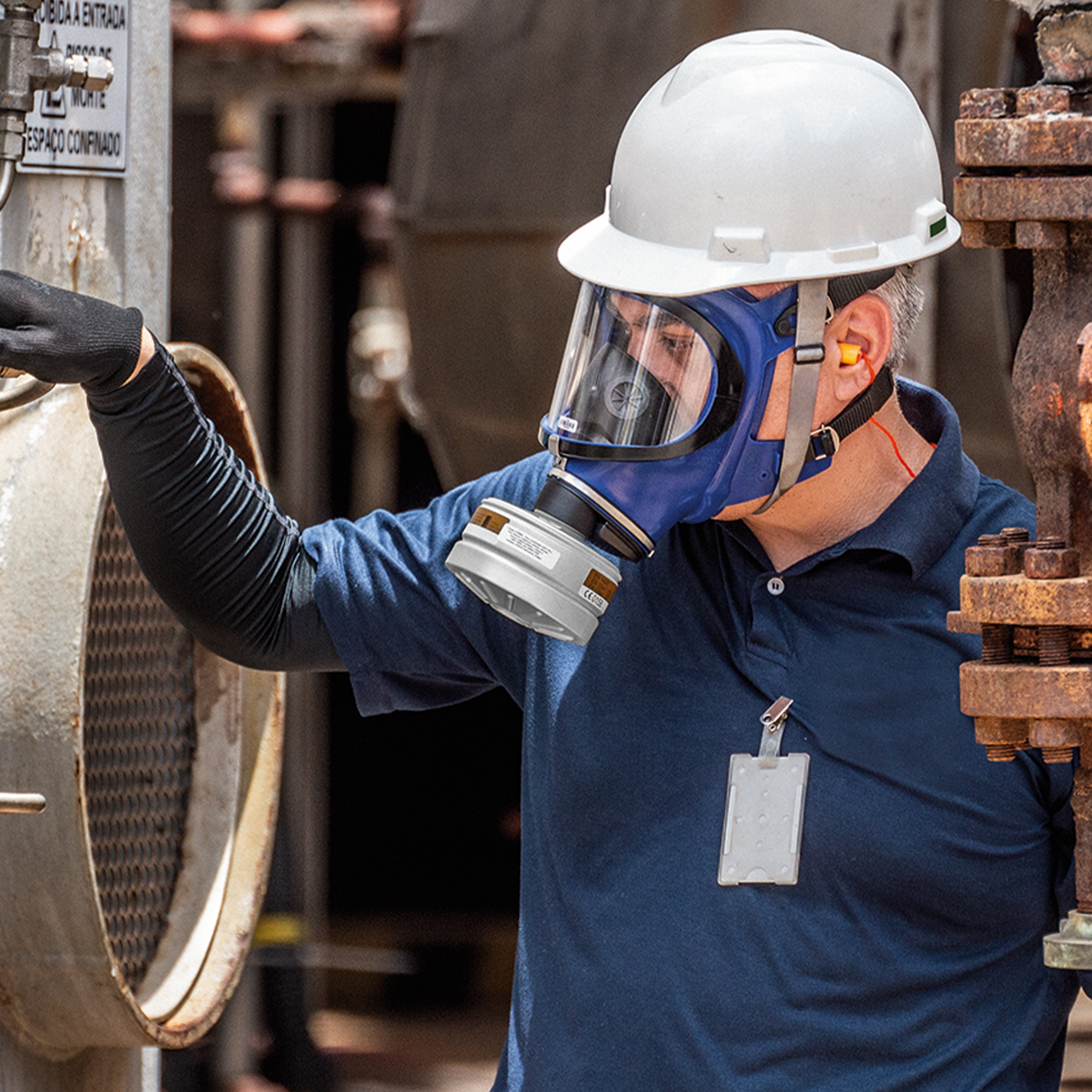 Arbeiter mit Helm und Atemschutzmaske in industrieller Umgebung.