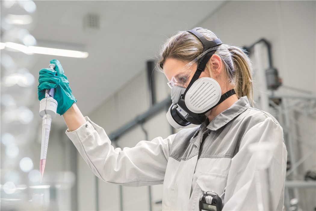 Sicherheitsausrüstung bei Laborarbeit Person im Labor mit Schutzmaske und Pipette in Aktion.