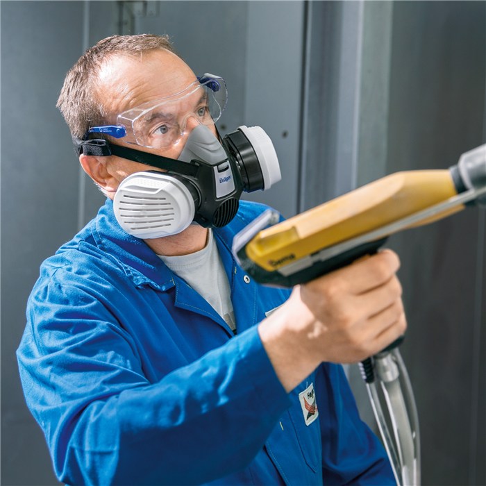 Schutzbrille Dräger X-pect 8120 Person in blauer Arbeitsjacke mit Atemschutzmaske und Schutzbrille arbeitet mit Gerät in technischer Umgebung.