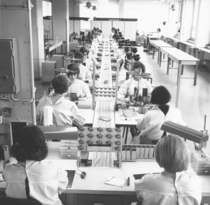 Röhrchenfertigung in den 1960er Jahren Frauen sitzen an langen Tischen in einer Produktionslinie für Röhrchen.