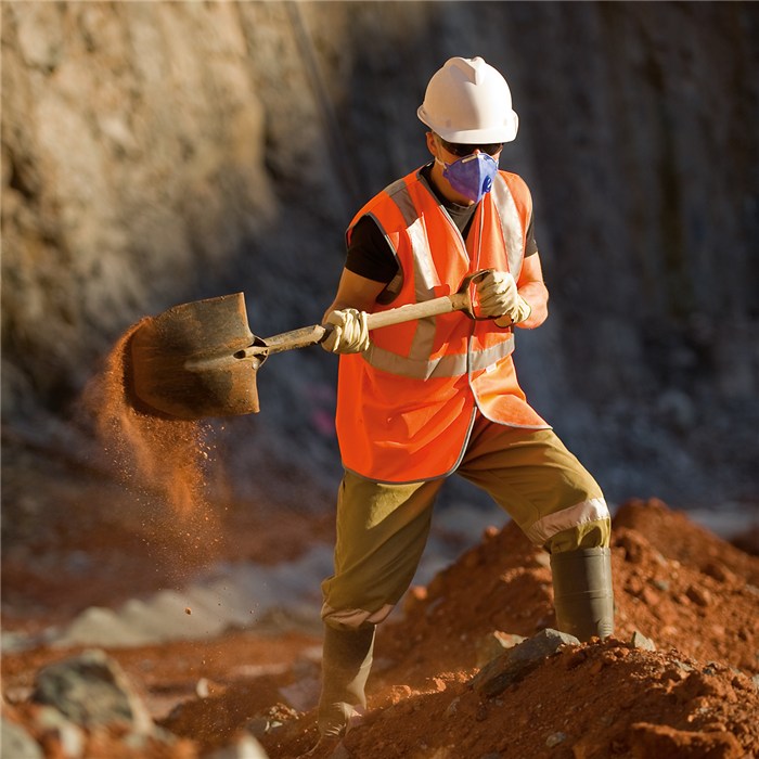 Atemschutzmaske auf Baustelle Eine Person trägt Schutzkleidung und arbeitet mit einer Schaufel auf einer Baustelle.