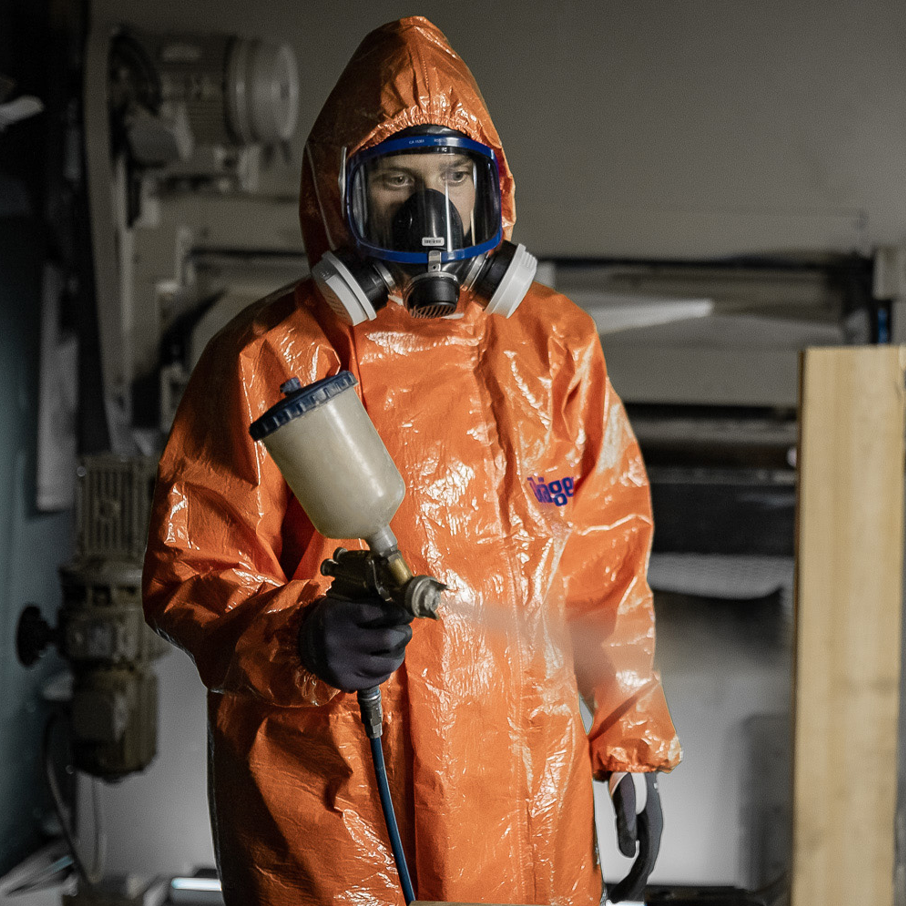 Sicherheitsanzug für Chemikalien Person im orangefarbenen Schutzanzug mit Atemschutz und Sprühgerät.
