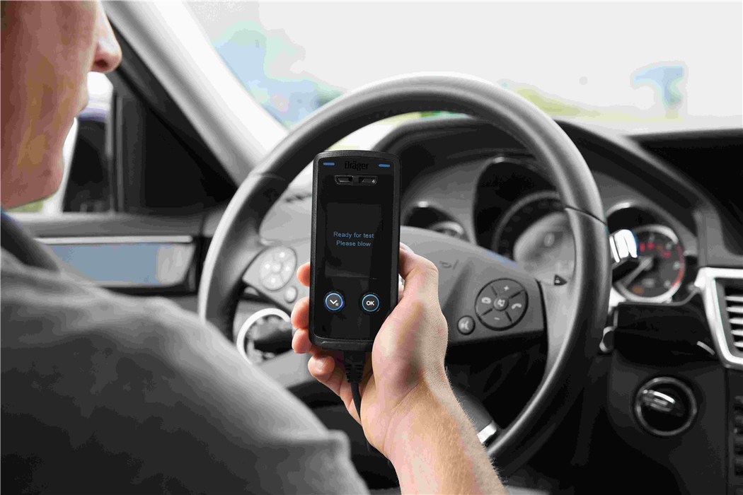 Interlock-Gerät zeigt an: Bereit zur Atemprobe Fahrer im Auto hält ein Alkohol-Interlock-Gerät, das zur Atemprobe auffordert.