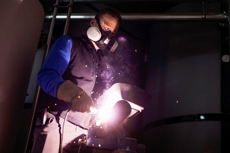 Sicherheit bei Schweißarbeiten mit Atemschutz Person mit Atemschutzmaske beim Schweißen, Funkenflug sichtbar.