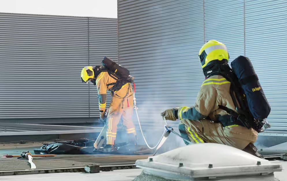 Zwei Feuerwehrleute mit Atemschutz auf einem Dach bei Löscharbeiten.
