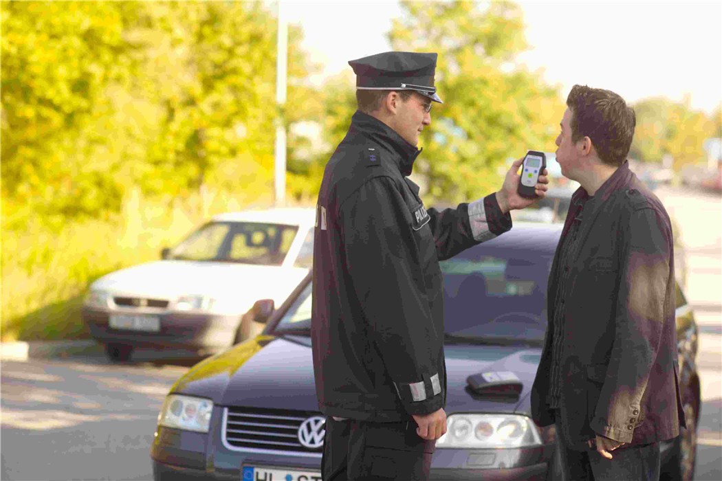 Alkoholtester im Einsatz bei Verkehrskontrolle Polizist benutzt Alkoholtestgerät bei Autofahrer. Fahrzeug im Hintergrund.
