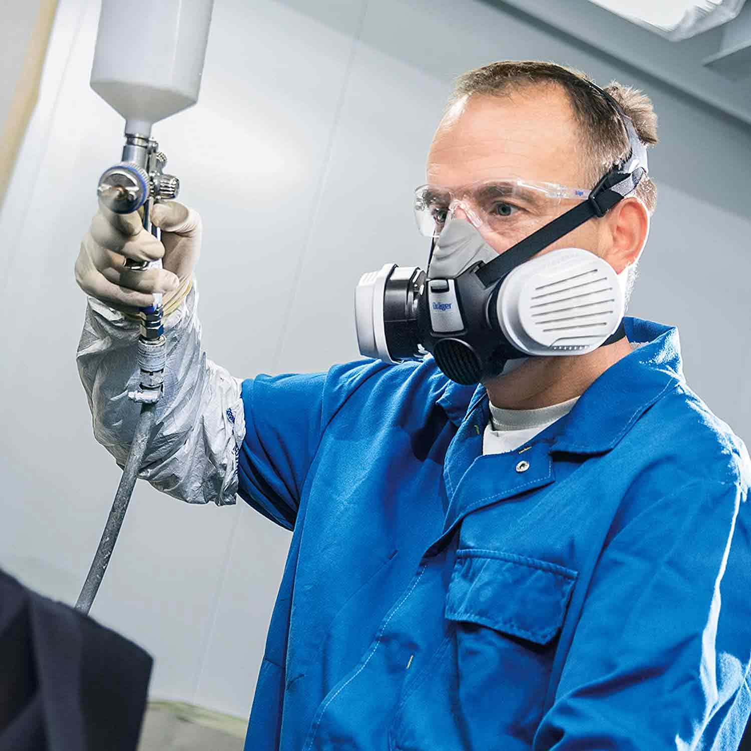 Person mit Filtermaske und Sprühgerät beim Lackieren.