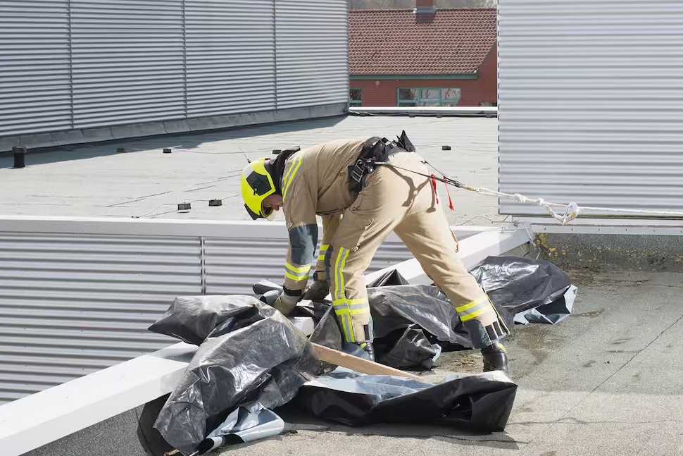 Feuerwehrmann in Schutzkleidung legt schützende Planen auf einem Flachdach aus.
