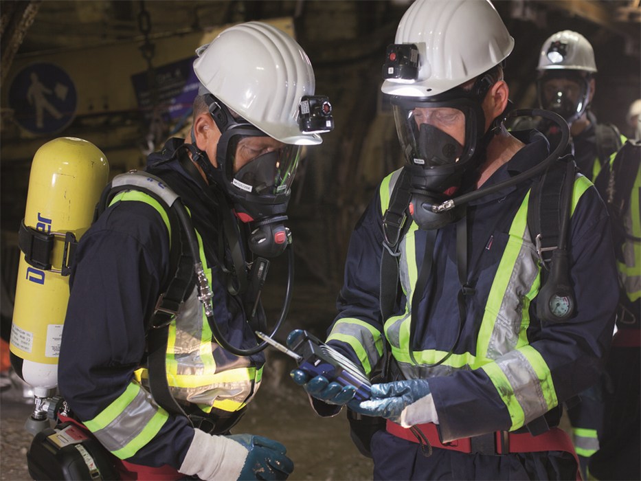Sicherheitstechnik im Einsatz Zwei Personen mit Sicherheitsausrüstung und Atemschutzgerät in einer industriellen Umgebung.