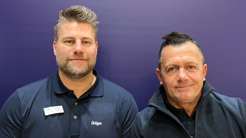 Dräger Unternehmensrepräsentanten Zwei Personen in Dräger-Bekleidung vor einem lila Hintergrund.