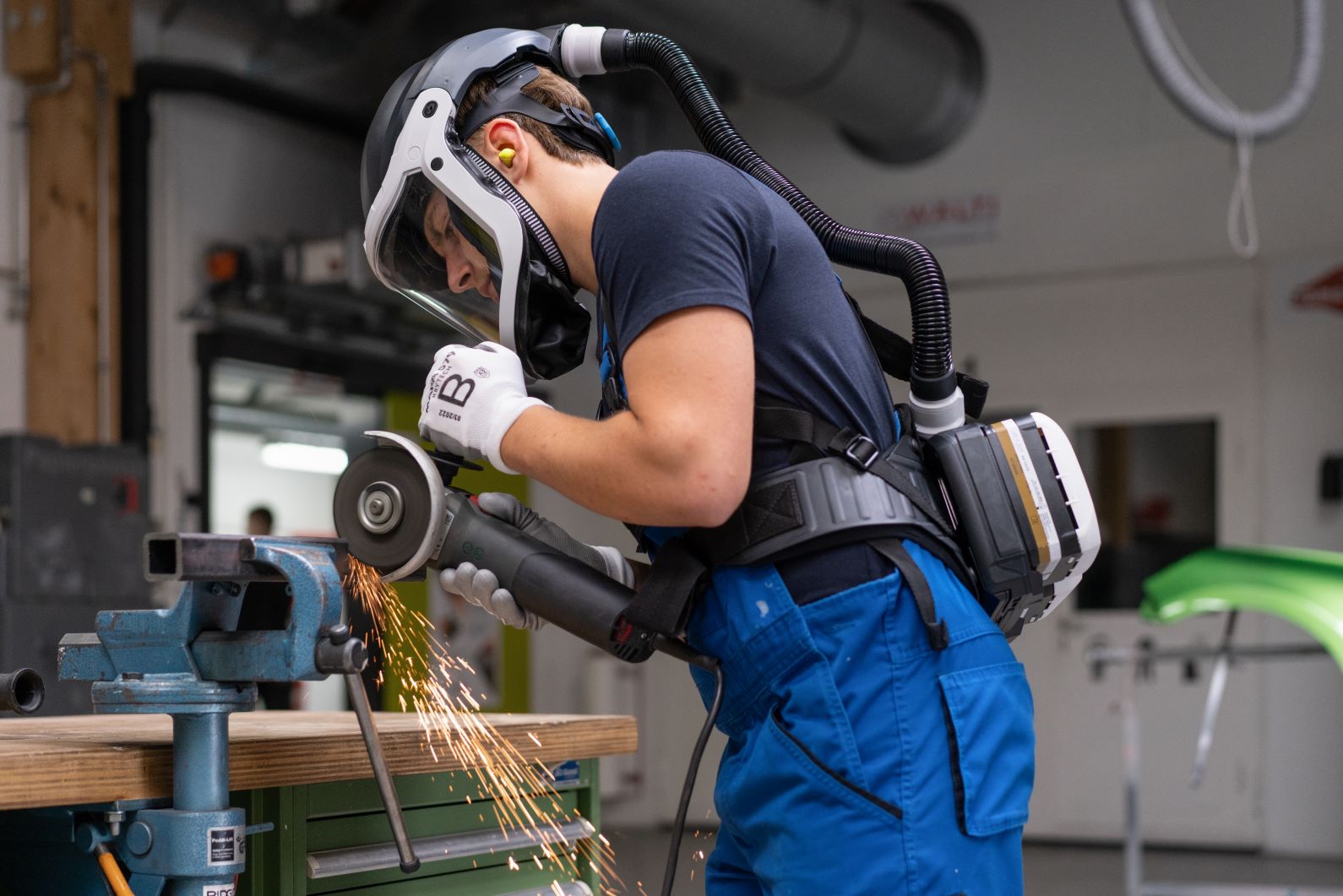 Schutzmaske mit Atemgerät bei Arbeitseinsatz Person in Schutzkleidung schleift Metallstück mit Atemschutz.