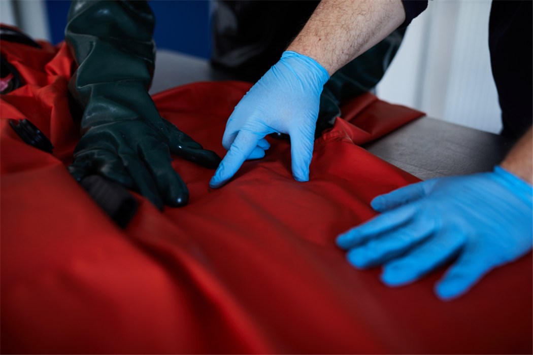 Hände mit Handschuhen begutachten roten Schutzanzug auf Tisch.