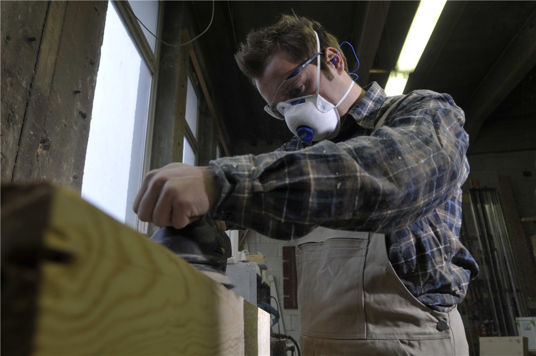 Handwerker mit Atemschutzmaske bei der Arbeit Ein Mann trägt eine Atemschutzmaske und schleift Holz.
