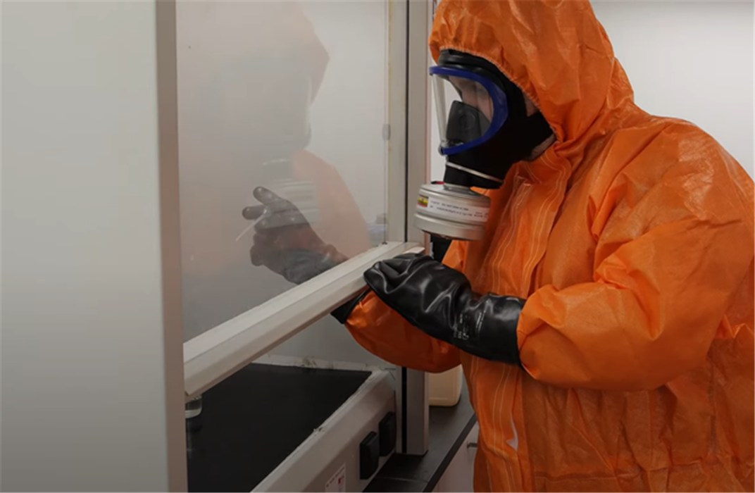 Sicherheitstechnische Schutzkleidung Person in orange Schutzanzug mit Atemmaske vor einer Laborablage.