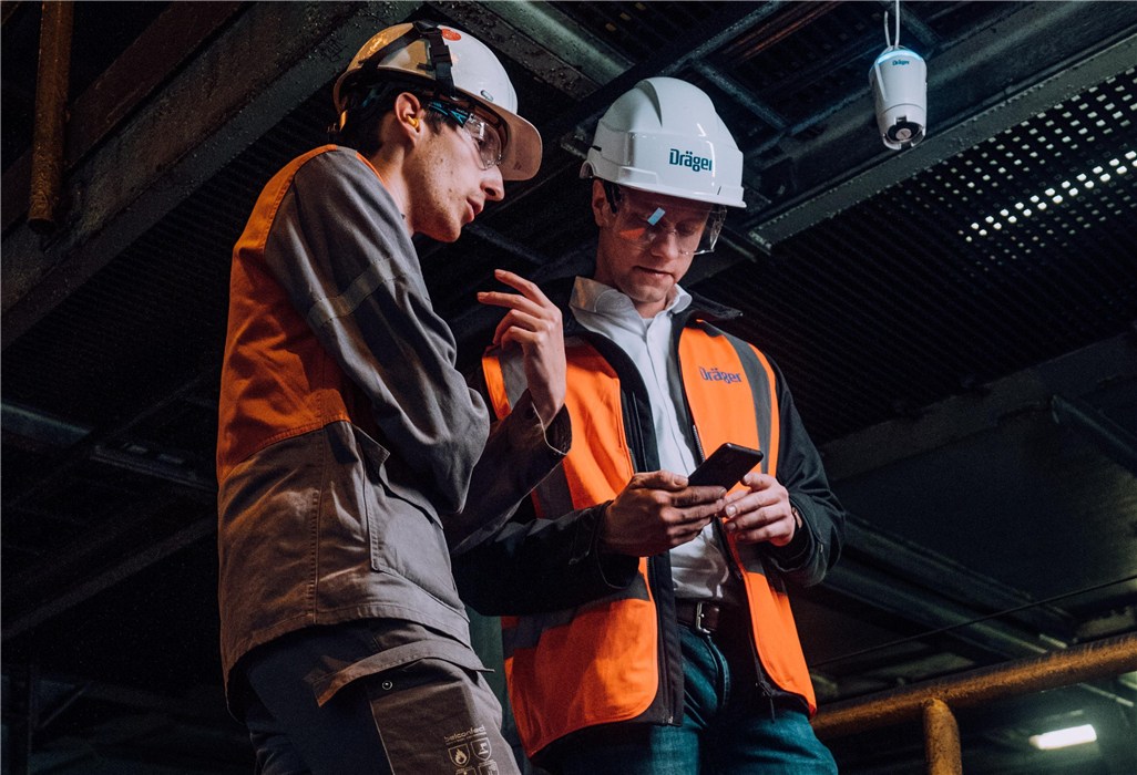 Zwei Personen in Sicherheitskleidung auf einer Baustelle, mit Helmen und Dräger Ausrüstung.