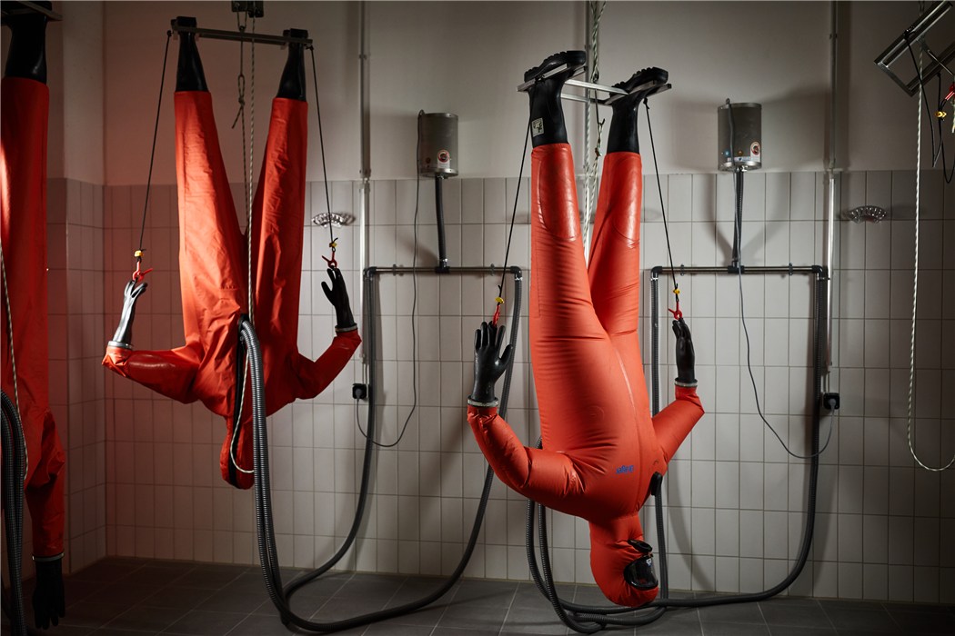 Zwei Personen in orangefarbener Sicherheitsausrüstung hängen kopfüber in einer Trainingsumgebung.