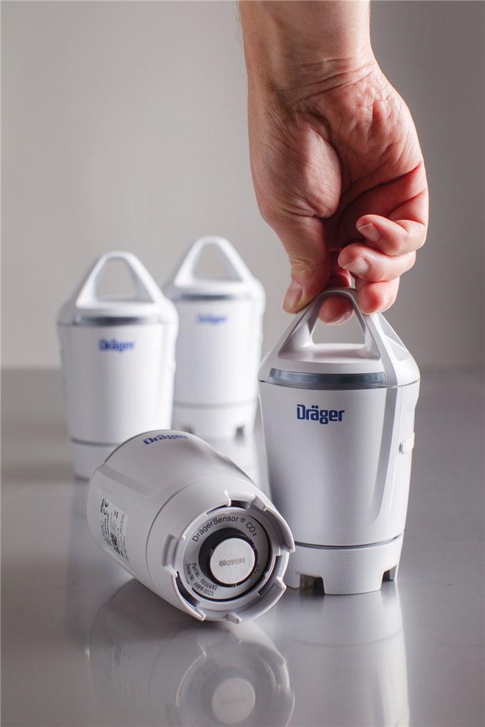 Hand hebt weißen Dräger Sicherheitssensor, weitere Sensoren stehen im Hintergrund.