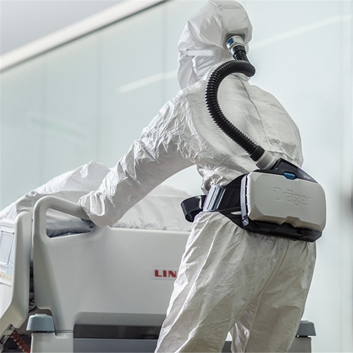 Dräger X-plore 8000 Haube in Aktion Person in Schutzanzug mit Atemschutzhaube, arbeitet an einem medizinischen Bett.
