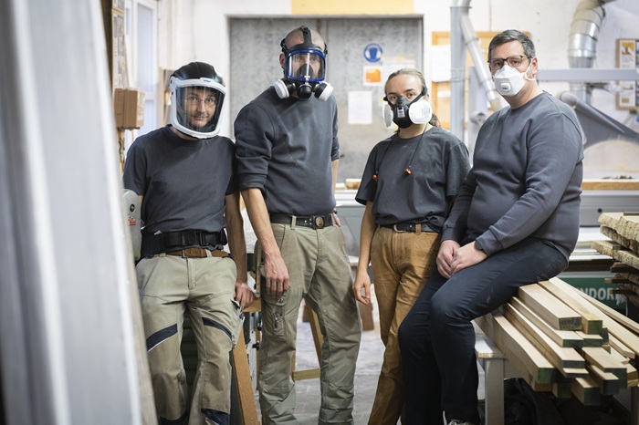 Vier Personen in Arbeitskleidung mit Atemschutzmasken.