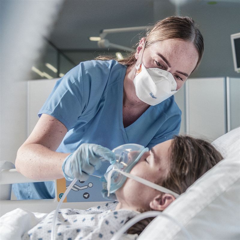 Atemschutzmaske X-plore in der Anwendung Pflegekraft setzt Patientin Atemschutzmaske auf.