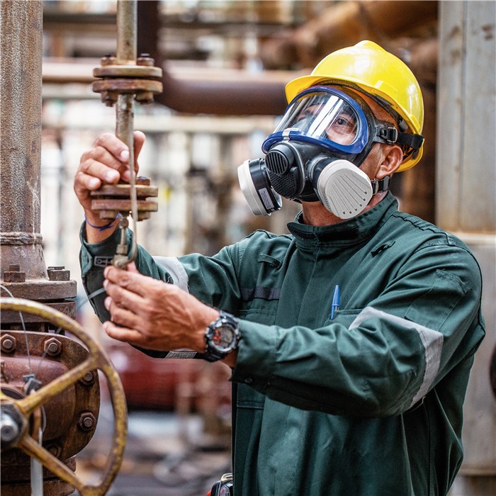 Arbeiter mit Atemschutzmaske und Schutzhelm Mann mit Schutzmaske und Helm bedient Ventil in Industrieumgebung.