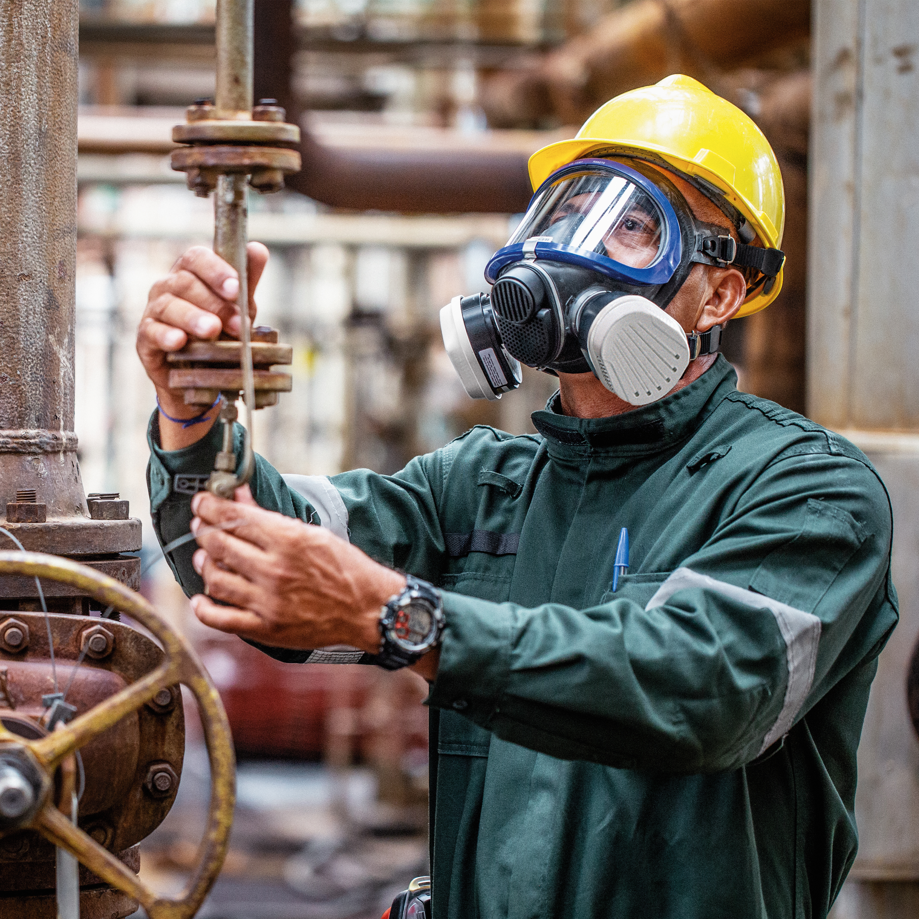 Arbeiter mit Atemschutzmaske und Schutzhelm Mann mit Schutzmaske und Helm bedient Ventil in Industrieumgebung.
