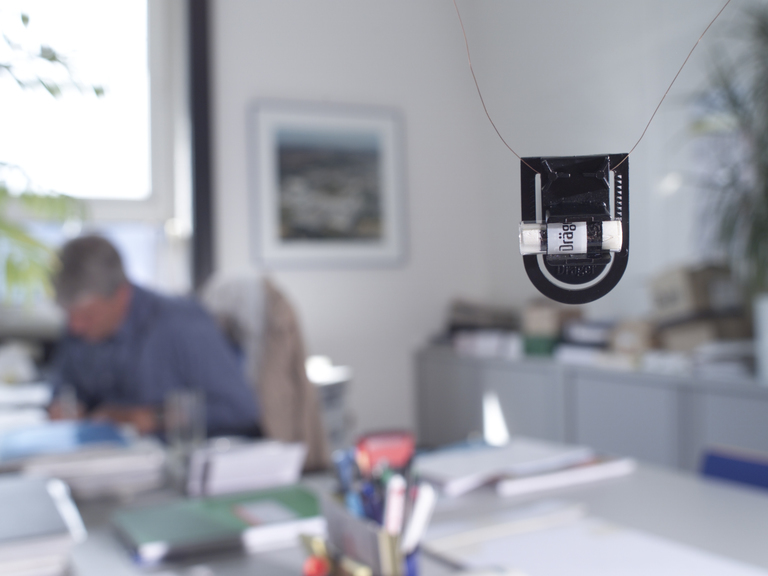 Dräger Sicherheitsgerät im Büro Ein Dräger Sensor hängt vor einem Büroarbeitsplatz mit unscharfer Person im Hintergrund.