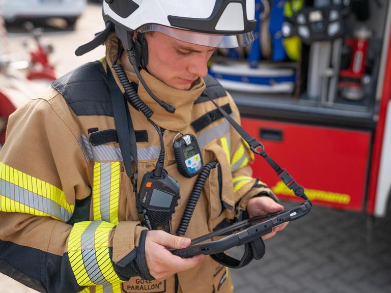 Feuerwehrmann nutzt Sicherheitsausrüstung Feuerwehrmann in Einsatzkleidung mit Funkgerät vor Einsatzfahrzeug.