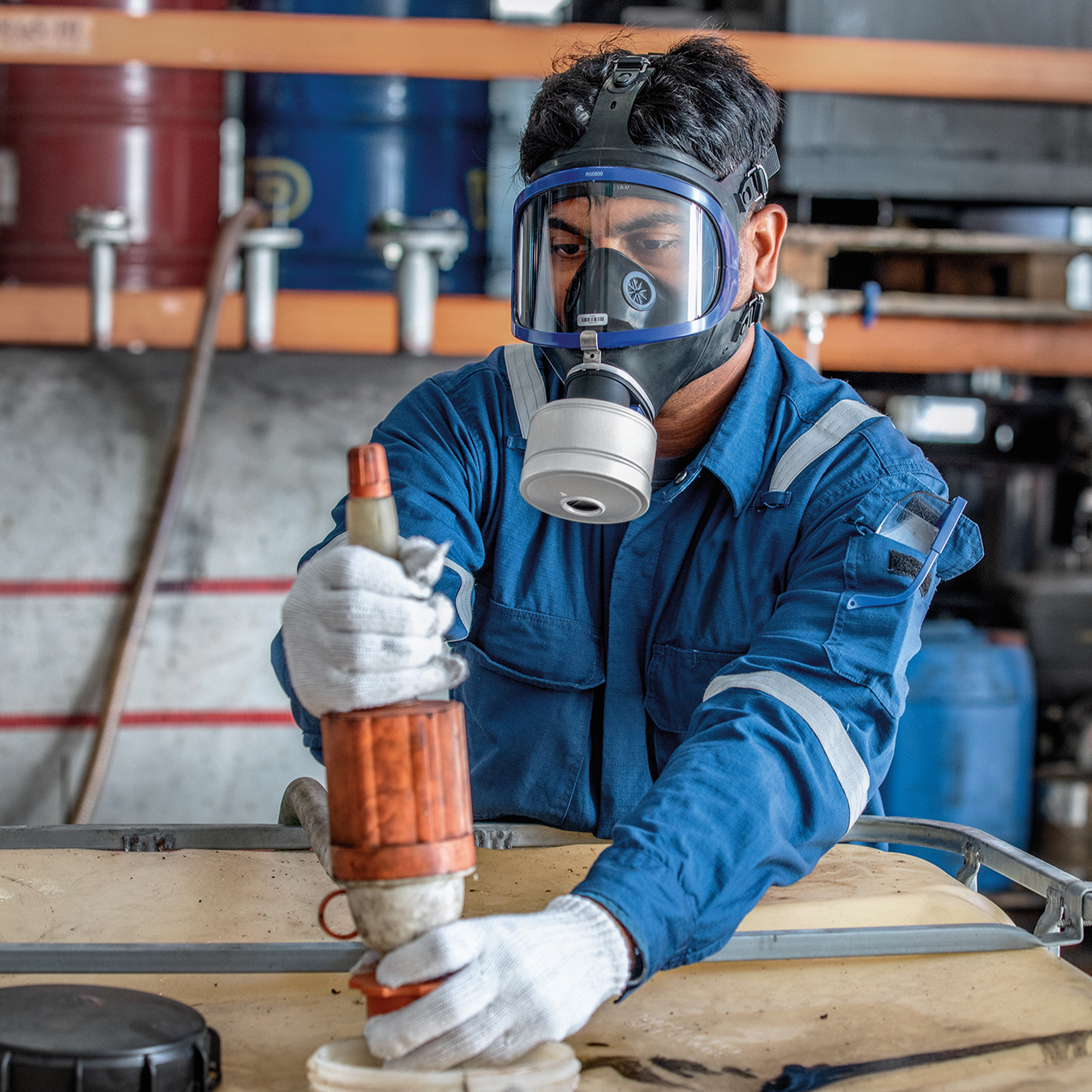 Arbeiter mit blauem Overall benutzt Atemschutzgerät bei der Arbeit mit einem Sicherheitsprodukt.
