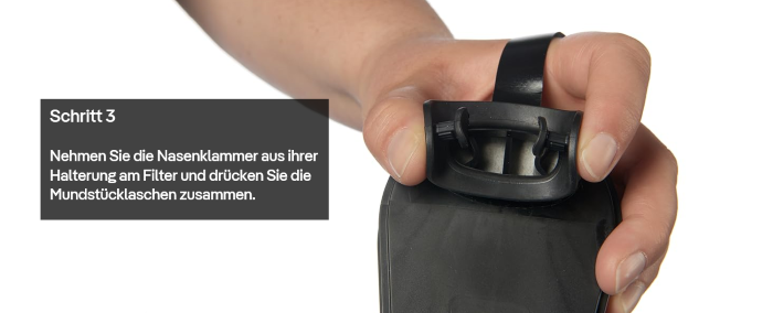 Hand drückt die Mundstückklammer eines Fluchtgeräts zusammen.