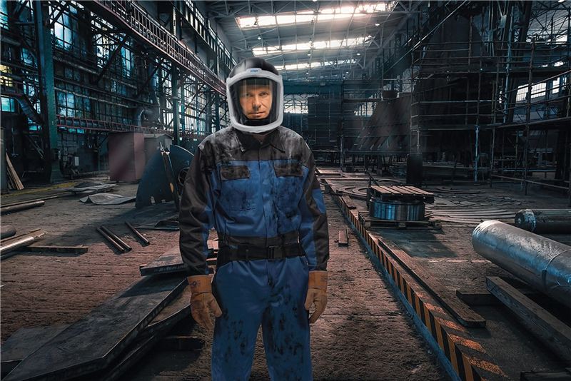 Schutzhelm mit Gesichtsschutz im Einsatz Person in Arbeitskleidung mit Schutzhelm in einer Fabrikumgebung.