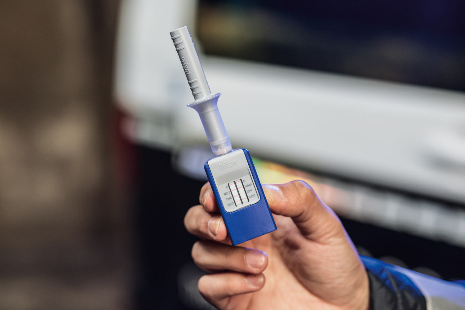 Dräger DrugCheck 3000 im Einsatz Hand hält das DrugCheck 3000 von Dräger vor einem Polizeifahrzeug.
