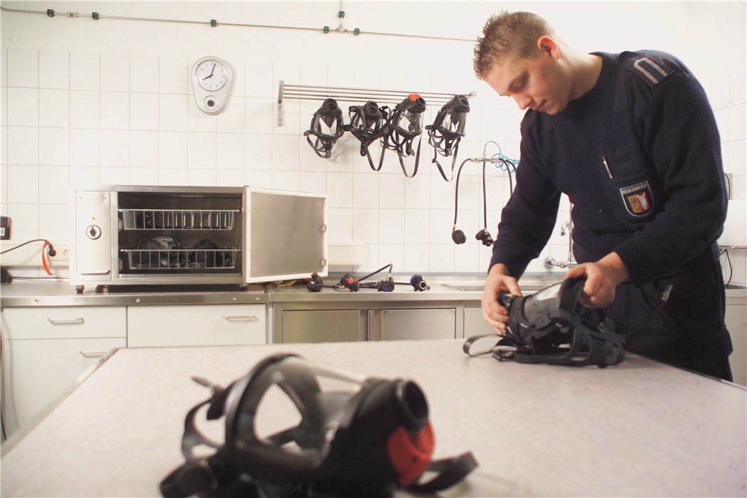 Schutzmasken werden in einem Labor von einem Polizisten gereinigt. Maskenhalterungen und Desinfektionsgerät im Hintergru