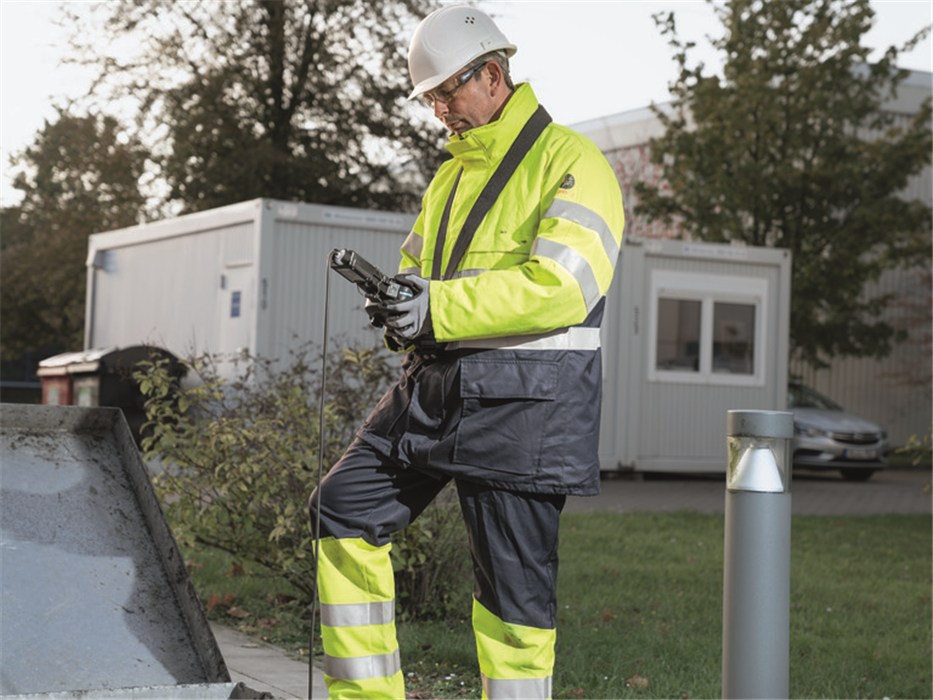 Sicherheitstechnik im Einsatz Person in Schutzkleidung mit Messgerät neben Grube.